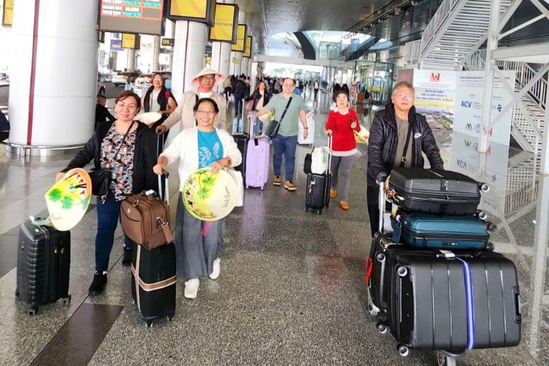 Guide and assistant coordinating headcount and luggage loading for two-coach departure after Vietnam airport arrivals
